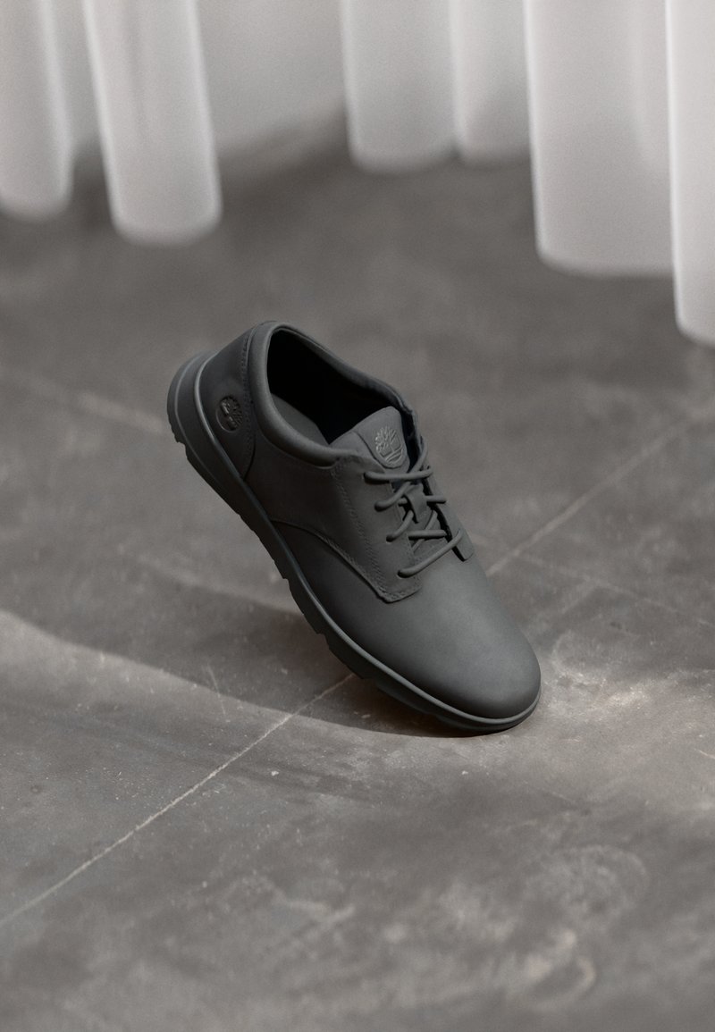 Zapatos de cuero negro con una textura suave, punta redonda y diseño de cordones. Detalle sutil del logo en el lateral y suela de goma.