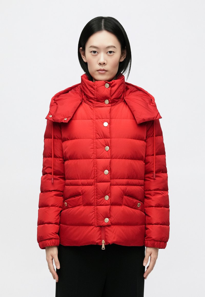 Rote gesteppte Jacke mit hohem Kragen, Druckknöpfen, Seitentaschen und abnehmbarem Kapuzen. Glatte Textur mit glänzendem Finish.