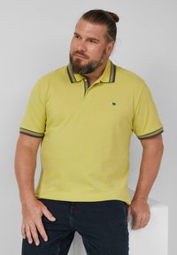 Poloshirt in leuchtendem Gelb mit strukturiertem Material, mit grau gestreiftem Kragen und Ärmelbündchen. Kleines Logo auf der linken Brust.