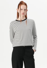 Camisa de manga larga a rayas en blanco y negro con cuello redondo, combinada con pantalones negros. La tela parece suave y tiene un corte relajado.