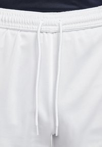 Pantalones cortos deportivos blancos con una cinturilla elástica y cuerdas blancas, usados con una parte superior oscura.
