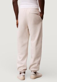 Lichtbeige sweatpants met een ontspannen pasvorm, elastische tailleband, omslagboorden bij de enkels en een achterzak. Zachte stof met een gladde textuur.