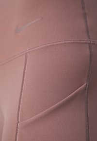 Gros plan sur un legging de sport mauve avec des coutures visibles et un logo Nike discret en haut à gauche.