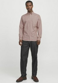Camisa de botones rosa claro con un bolsillo en el pecho, mangas largas, combinada con jeans de mezclilla oscura y zapatos marrones. Diseño simple y corte relajado.