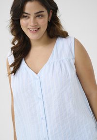 Haut sans manches bleu clair avec des rayures verticales blanches, décolleté en V et fermeture par boutons sur le devant ; fabriqué en tissu en coton texturé.