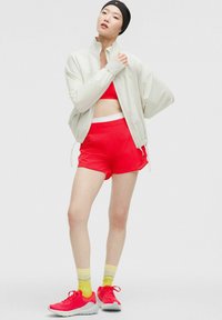 Conjunto atlético que incluye una chaqueta de punto gris claro con cremallera, un top corto rojo, pantalones cortos rojos y zapatillas rosas con calcetines de rayas amarillas. Materiales suaves.