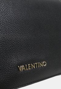 Borsa a mano in pelle nera con superficie texturizzata e logo "VALENTINO" dorato sul davanti, caratterizzata da una forma rettangolare elegante.