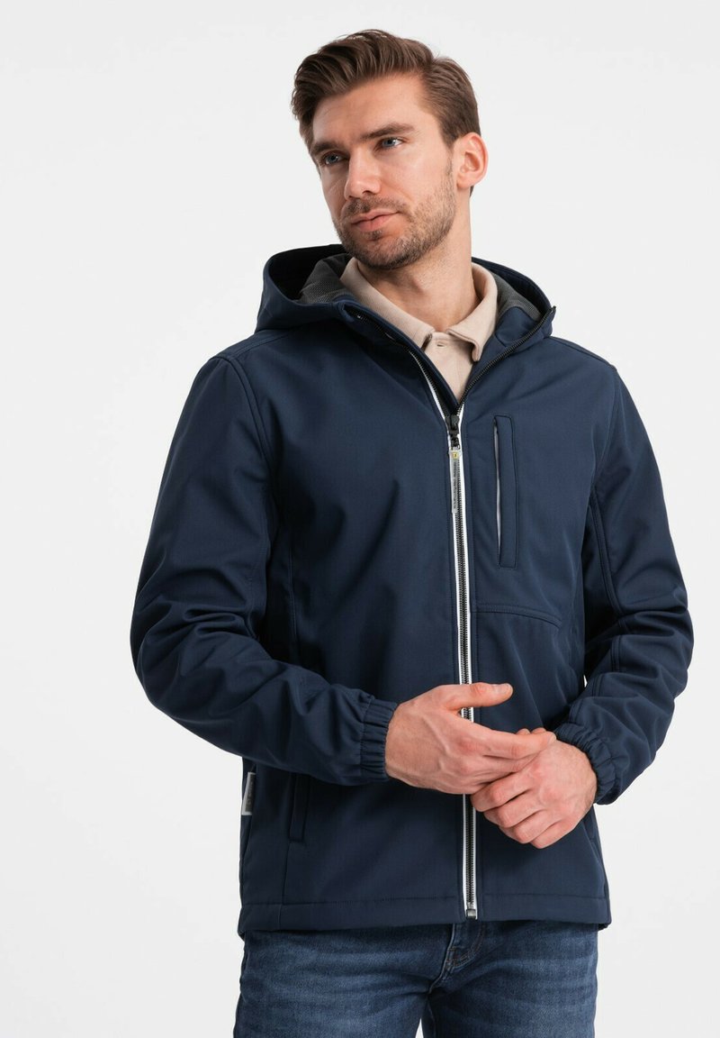 Marineblå hættejakke lavet af glat stof, med en lynlåsåbning foran, elastiske håndled og en lynlåslomme på brystet.