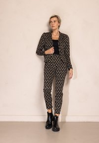 Schwarzes und beiges Blazer- und Hosen-Set mit geometrischem Muster, taillierter Silhouette, kombiniert mit schwarzen Stiefeletten.