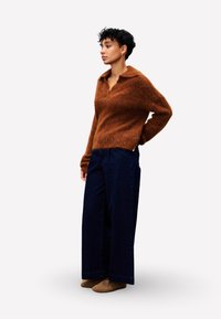 Brauner, flauschiger Pullover mit Kragen, kombiniert mit weiten, dunklen Jeans. Das Outfit hat eine lockere Passform und strukturierte Stoffe.