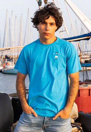 T-shirt in cotone azzurro chiaro con collo a giro, maniche corte e un piccolo design ricamato sul lato sinistro del petto. Indossato con jeans in denim chiaro.