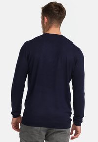 Suéter ligero azul marino con cuello redondo, mangas largas y puños acanalados; textura suave, diseño minimalista, sin patrones visibles.