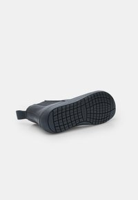 Černá kožená bota s texturovanou gumovou podrážkou, poutkem na patě a vzorkem na podrážce ve tvaru cik-cak. Jednoduchý design, vhodný pro různé příležitosti.