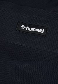 Granatowy dzianinowy materiał o prążkowanej fakturze. Zawiera wyraźną czarną metkę z białym logo "hummel" przyszytą na niej.