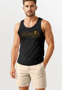 Schwarzes Tanktop mit einem Grafikmotiv von einem orangefarbenen Berg und der Sonne. Hergestellt aus einem Stoff mit glatter Textur. Modell trägt hellfarbene Shorts.