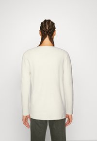 Sweter z długim rękawem i okrągłym dekoltem w jasnobeżowym kolorze, wykonany z teksturowanej dzianiny. Charakteryzuje się luźnym krojem, widocznymi szwami i prostym dołem.