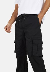 Czarne spodnie cargo o luźnym kroju, z elastycznym pasem i sznurkiem do regulacji oraz wieloma bocznymi kieszeniami. Wykonane z lekkiego materiału.