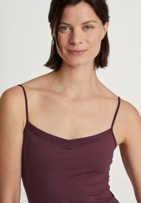 Bordeaux camisole met dunne verstelbare spaghettibandjes en een V-vormige halslijn. Gemaakt van zachte stof, met een gladde textuur en een minimalistisch ontwerp.