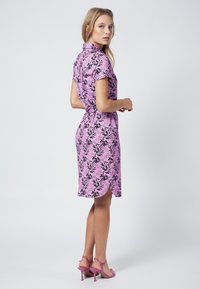 Abito rosa con un motivo floreale nero, maniche corte e orlo curvo. Indossato con sandali a tacco alto rosa coordinati.