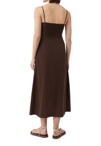 Braunes, ärmelloses Maxikleid mit gerafftem Oberteil und gerader Silhouette, kombiniert mit flachen Riemchensandalen. Weicher Stoff mit minimaler Textur.