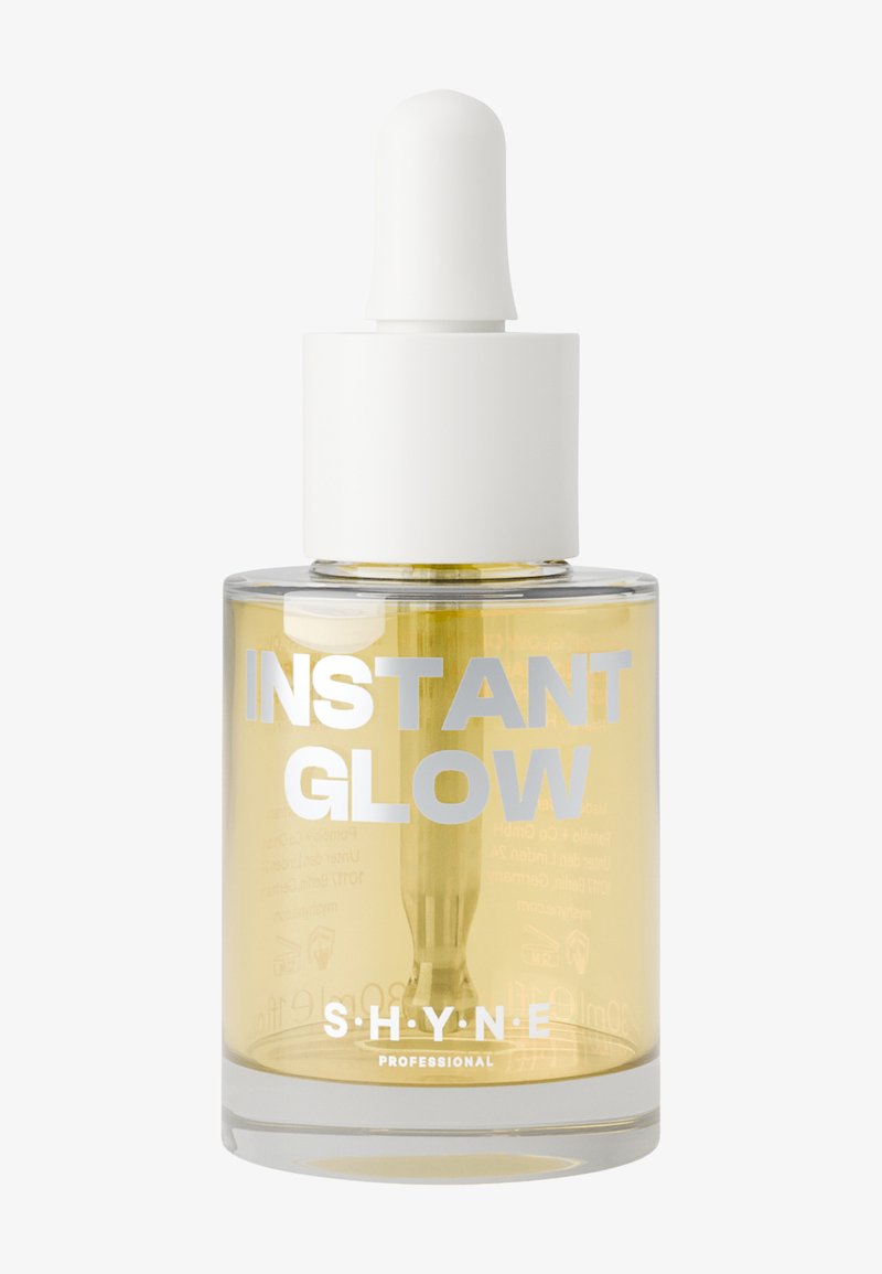 Klar glasflaska som innehåller gul serum, med ett vitt dropplock. Etiketter med texten "INSTANT GLOW" och "S.H.Y.N.E PROFESSIONAL" i silver.