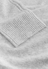 Sivá pletená tkanina svetra s textúrovaným rebrovaným akcentom na manžete. Mäkká, chlpatá textúra v celej látke.