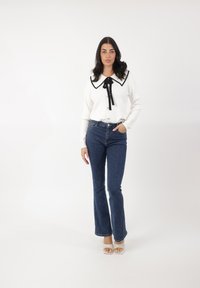 Suéter blanco con ribetes negros y gran cuello, con cierre de botones, combinado con jeans acampanados azules y sandalias de tacón blancas. Textura suave.