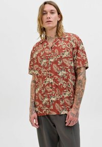 Camisa de botones de manga corta en color óxido con un patrón floral en crema y verde, que presenta un corte relajado y un cuello plano.