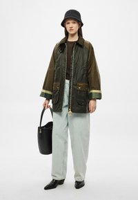 Πράσινο και καφέ βαμβακερό μπουφάν με κερί, με φερμουάρ μπροστά, δύο πατούρες τσέπης και καφέ γιακά. Συνδυασμένο με ανοιχτό μπλε τζιν και μαύρες μπότες.