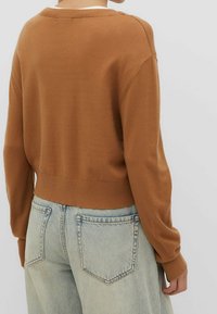 Suéter de punto marrón con un corte relajado y puños acanalados, combinado con unos jeans de corte relajado en azul claro que cuentan con bolsillos traseros.