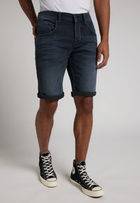 Pantalones cortos de mezclilla en azul oscuro con dobladillos enrollados, que presentan un estilo de cinco bolsillos y un ajuste regular, combinados con zapatillas negras de caña alta.