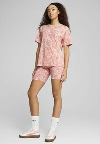 Pink camouflage athletic outfit featuring a relaxed fit short-sleeve shirt and matching bike shorts, paired with white sneakers and socks.