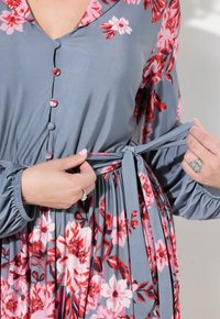 Květinové šaty v šedé barvě s růžovými a červenými vzory, s knoflíky a stahovacím pasem. Dlouhé, nabírané rukávy s elastickými manžetami. Měkká textura.
