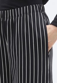 Pantalon à rayures verticales noires et blanches, doté d'une taille élastique et de poches latérales, fabriqué en tissu doux et léger.