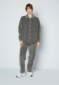 Szara koszula z kordurowego materiału z dużymi guzikami, w połączeniu z pasującymi spodniami. Posiada luźny krój i miękką teksturę. Noszona z białymi trampkami.