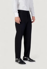 Pantaloni neri su misura realizzati in tessuto leggero, dotati di chiusura con zip e bottone. Abbinati a sneaker nere per un look informale.