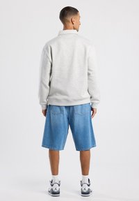 Felpa in pile grigia chiara con colletto ripiegato, abbinata a pantaloni corti in denim blu. Cuciture visibili e tasche laterali sui pantaloni.