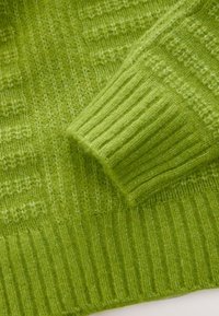 Tissu tricoté vert vif avec détail de poignets côtelés et motifs de points verticaux et diagonaux texturés.