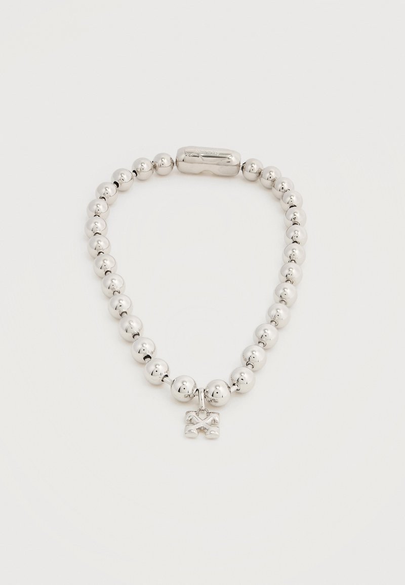 Bracelet en perles d'argent avec un petit pendentif en forme de tibias croisés et une fermeture magnétique sur un fond blanc uni.