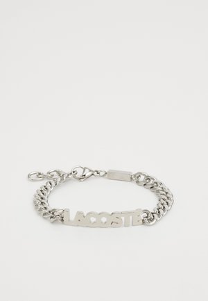 Hõbedane metallist ahelakäevõru keskel "LACOSTE" logo, varustatud katkupüüdja ja vastupidava, poleeritud viimistlusega.