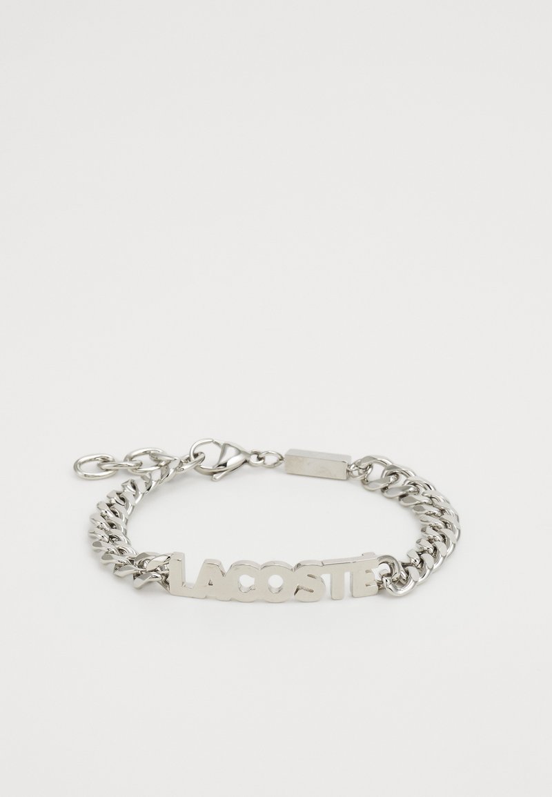Kjede armbånd laget av sølvmetall, med en sentral "LACOSTE"-logo, lås med hummerlås og en slitesterk, polert overflate.