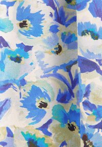 Motif floral bleu et turquoise avec centres noirs sur tissu blanc texturé, montrant plis et ombrages pour la profondeur et la dimension.