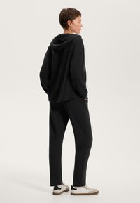 Čierna mikina s voľným strihom, predná kapsa a šnúrka; v kombinácii s čiernymi zúženými nohavicami. Biely tenisky s čiernymi akcentmi.