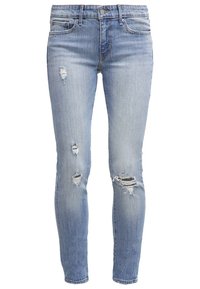Light blue, fitted denim jeans with distressed details. Features multiple ripped areas, a standard five-pocket design, and a classic zipper fly.