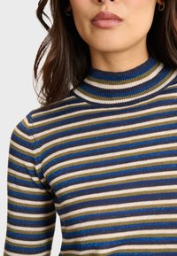 Gestreifter Strickoberteil mit hohem Kragen. Der Stoff zeigt grüne, marineblaue und silberne Streifen mit einer subtilen Schimmertextur.