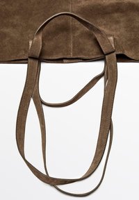 Brun mockasinväska med två långa, platta remmar. Har en slät yta och synlig sömnad längs kanterna. Öppen toppdesign.