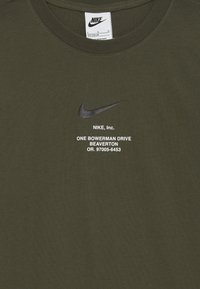 Tamsiai žalia medvilnės marškinėliai su juodu Nike swoosh logotipu ir balta tekstine informacija apie įmonės adresą. Apykaklė suapvalinta, trumpomis rankovėmis.