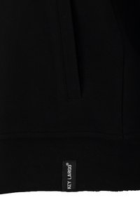 Sudadera negra con un tejido texturizado, bolsillo tipo canguro y una etiqueta que dice "KEY LARGO" en el dobladillo.