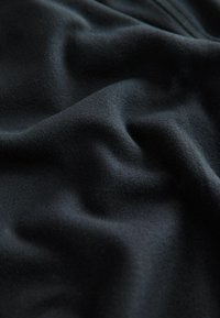 Tejido de forro polar negro con una textura suave y lisa, que presenta suaves ondulaciones y pliegues, adecuado para prendas de vestir o aplicaciones textiles.