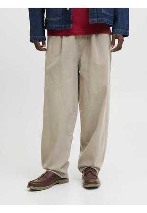 Person wearing beige wide-leg trousers, brown leather shoes, a red shirt, and a blue denim jacket against a plain background.